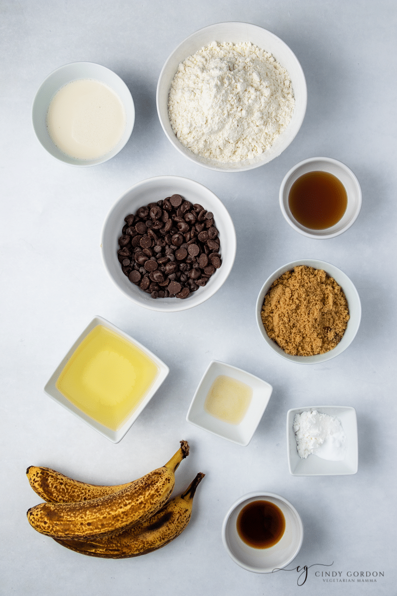 Spotty bananas next to bowls of flour, brown sugar, oil, salt, vanilla extract, and chocolate chips