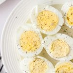 A plate of halved hard boiled eggs sprinkled with black pepper