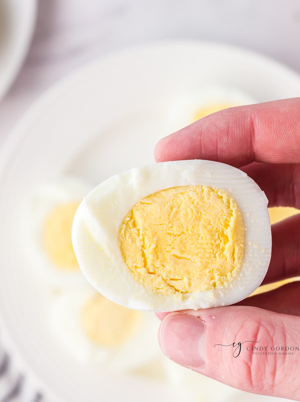 a hand holding half of a  hard boiled egg that is perfectly cooked. 