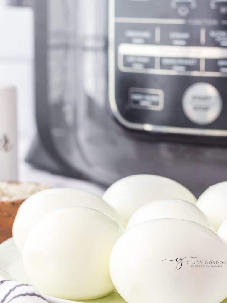 A plate of hard boiled eggs in front of a ninja foodi pressure cooker