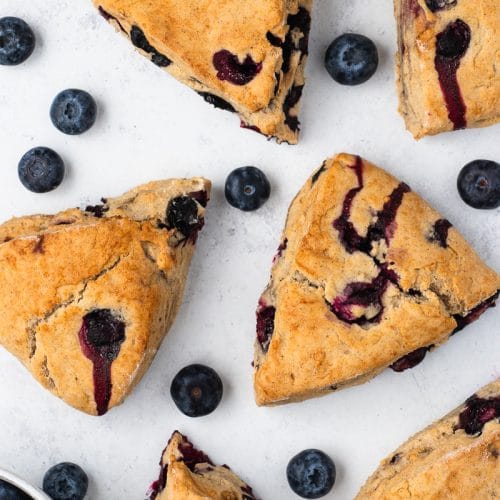 overhead view of a tray of triangular vegan blueberry scones with fresh blueberries scattered around.