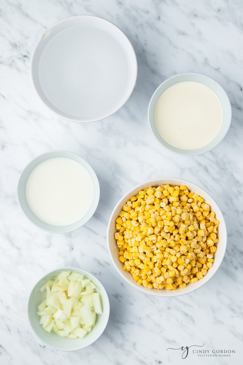 The five ingredients needed to make corn potage, measured out into separate bowls on a marble countertop