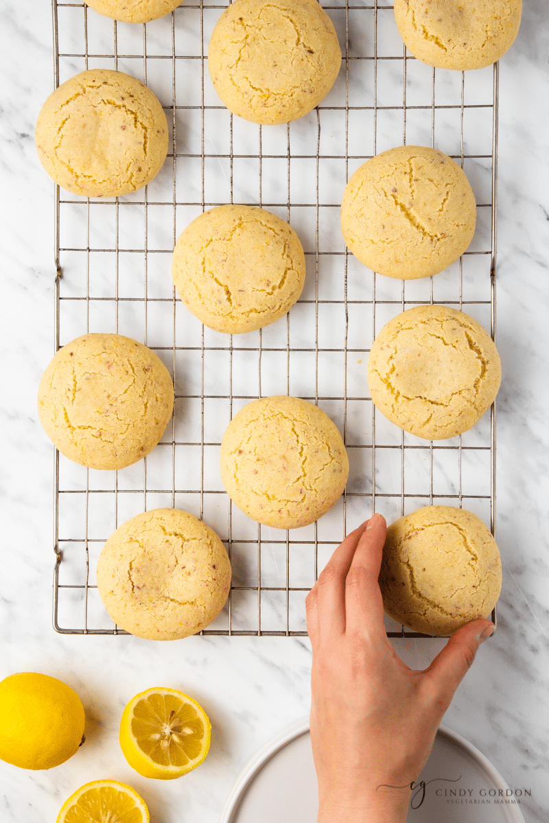 vegan lemon cookies on a cooling rack, overhead shot with black and white striped towel and a hand reaching for the cookies