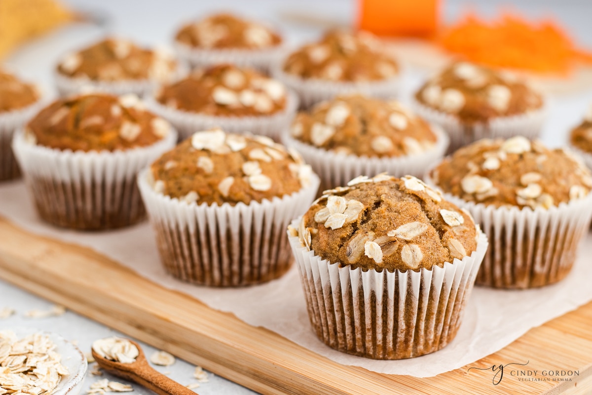 side view of brown muffins in white liners on top of parchment paper on top of a wooden cutting board