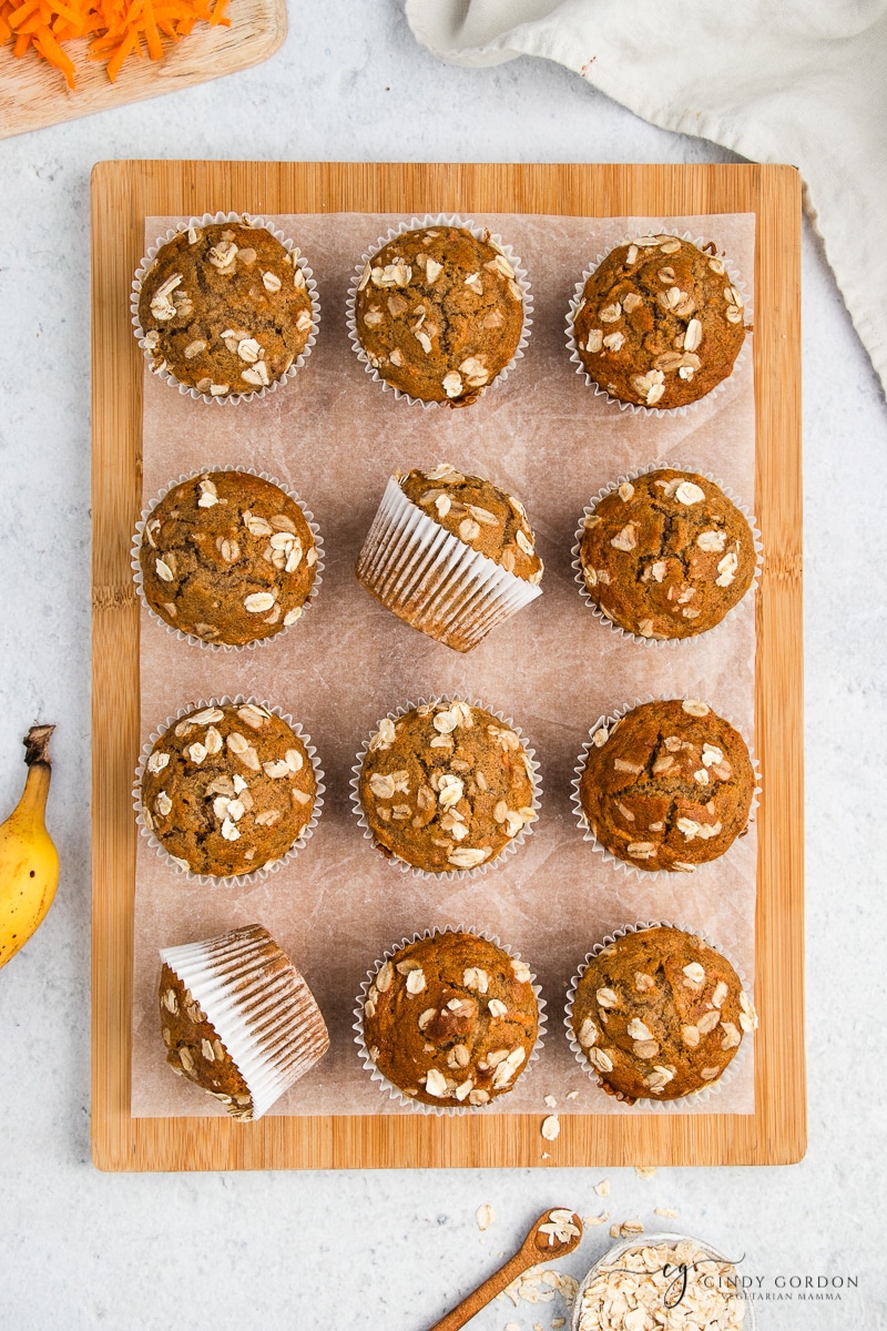 Overhead view of banana carrot muffins in white muffin liners on a wooden cutting board