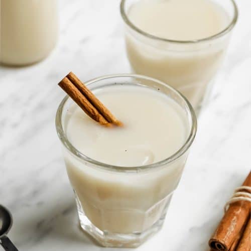 two glasses of creamy vegan horchata with cinnamon stick stirrers
