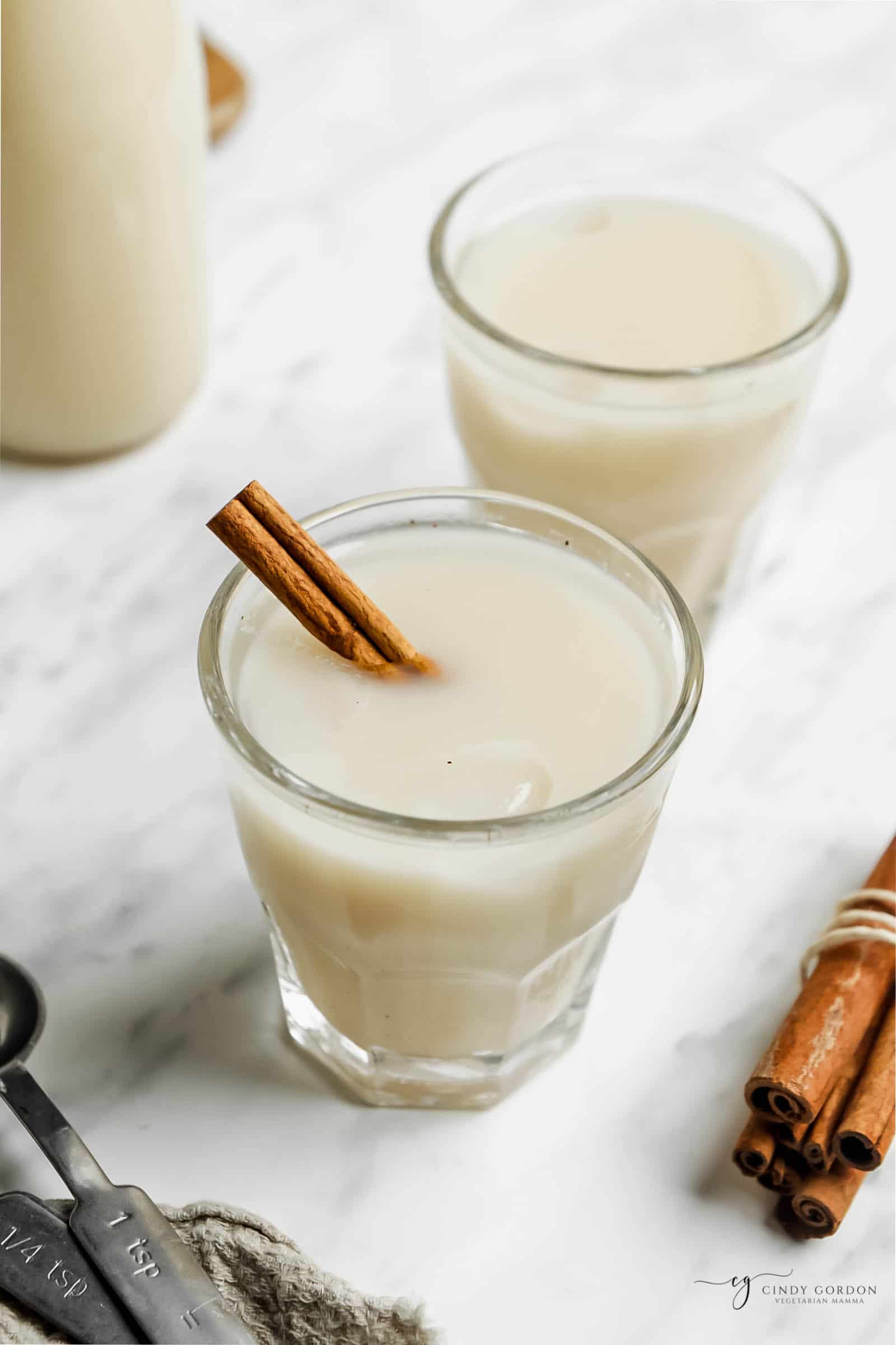 two glasses of creamy vegan horchata with cinnamon stick stirrers