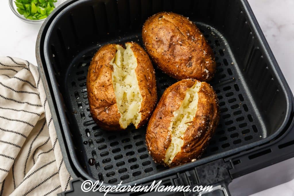 three air fryer baked potatoes in black air fryer pan.