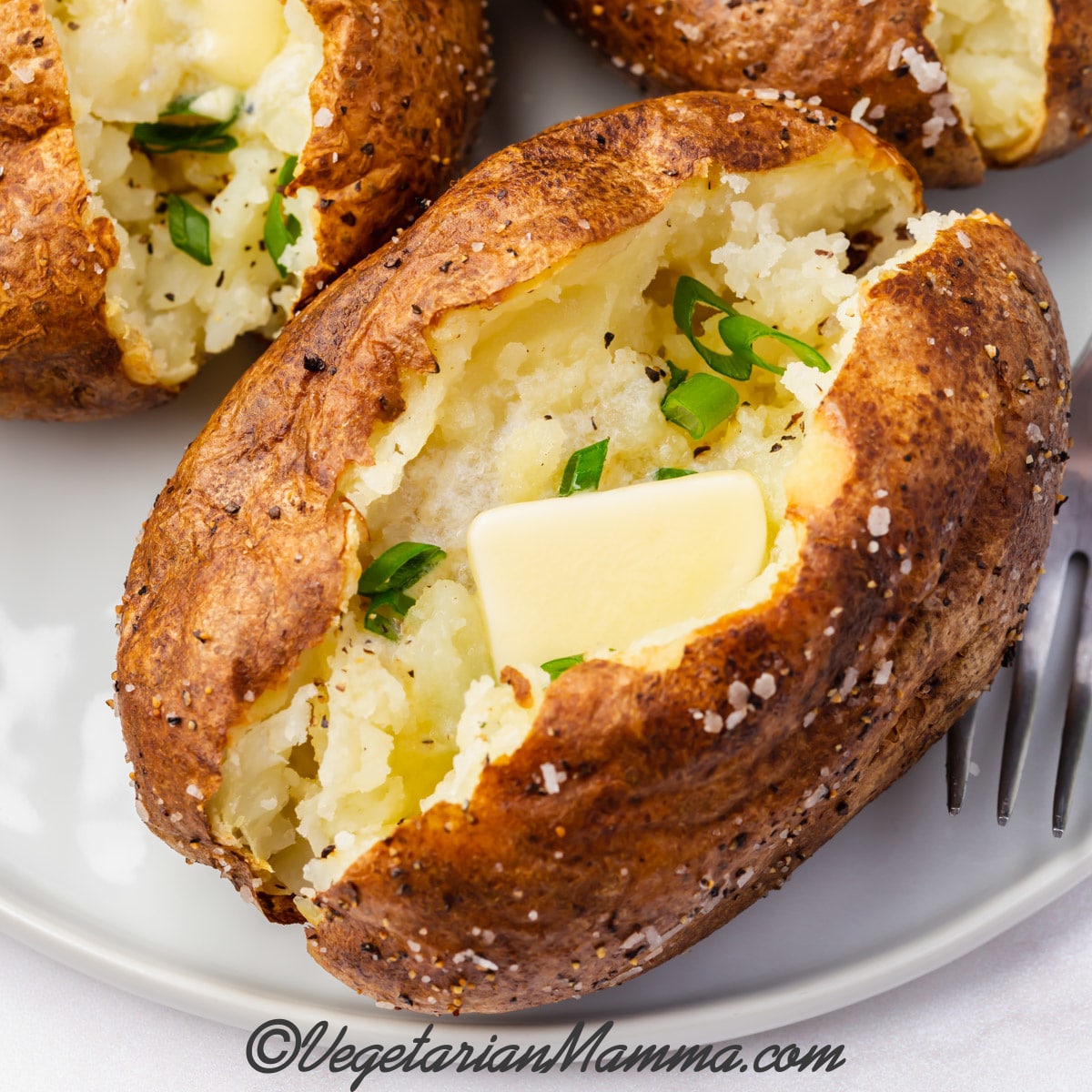 Baked potato with butter and chives on a plate.