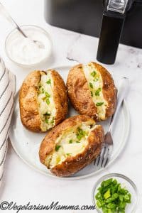 three air fryer baked potatoes with butter and chives with a bowl of sour cream.