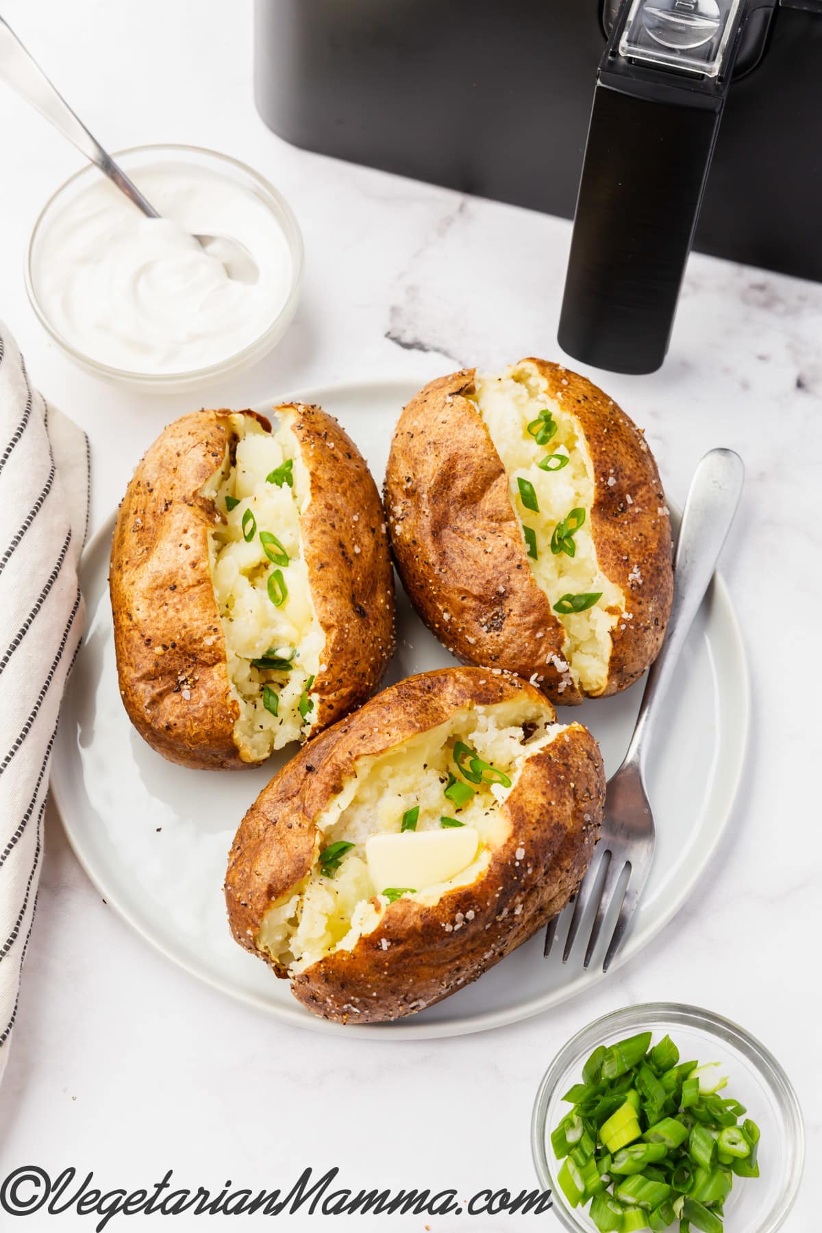white baked air fryer baked potatoes opened to add butter and chives on a white plate.
