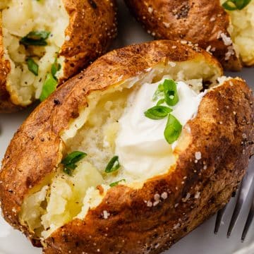 air fried baked potato with butter and chives on a plate.