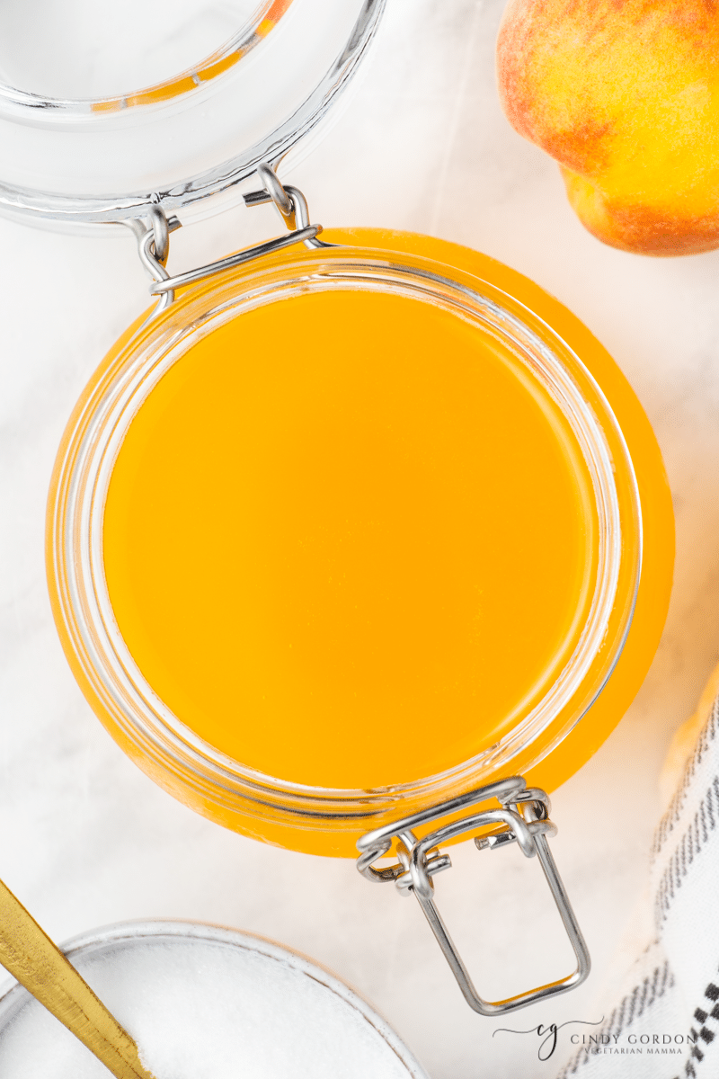 view from above of an open bail jar of peach syrup on a marble counter. 