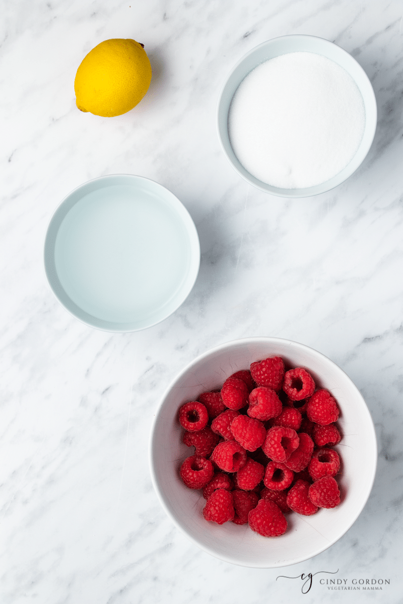 The ingredients for raspberry simple syrup, measured into separate bowls on a marble counter, viewed from above