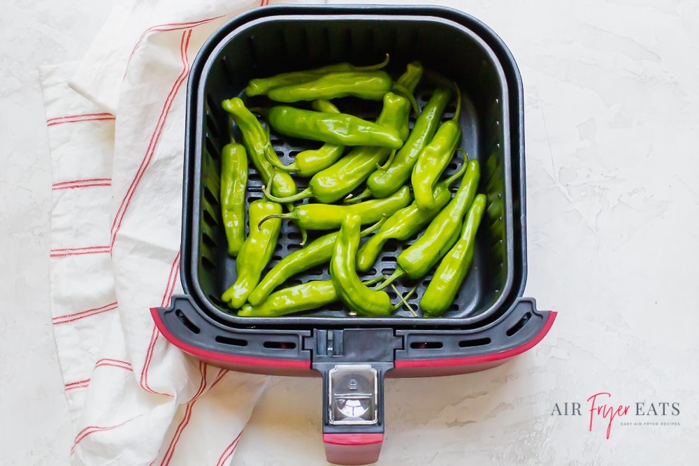 shishito peppers air fryer - blisted green long pepeprs in red and black air fryer basket