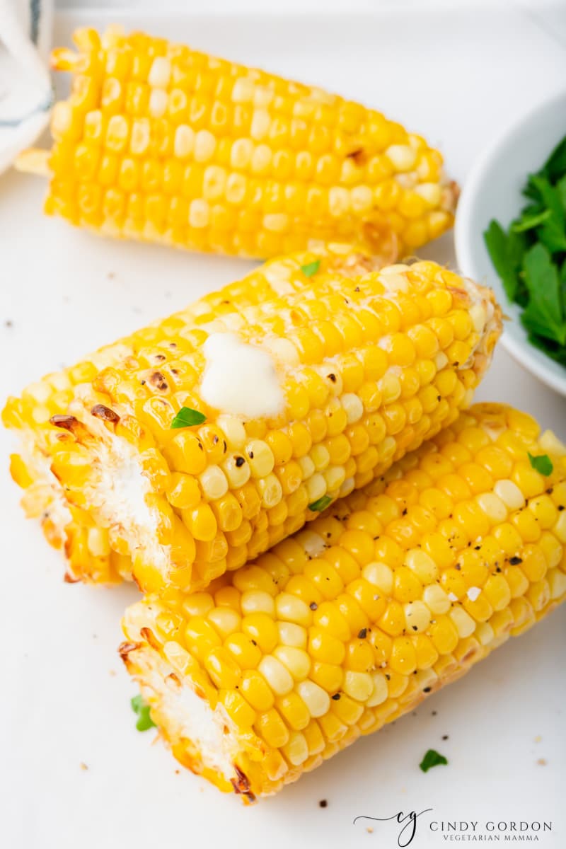 three pieces of air fryer corn with butter and some seasoning on it on a white plate