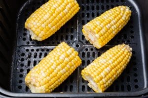 4 mini ears of corn in black air fryer basket, corn is raw