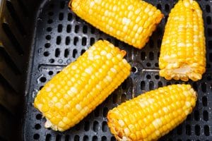4 pieces of cooked air fryer corn on the cob in black air fryer basket