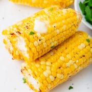 three pieces of air fryer corn with butter and some seasoning on it on a white plate