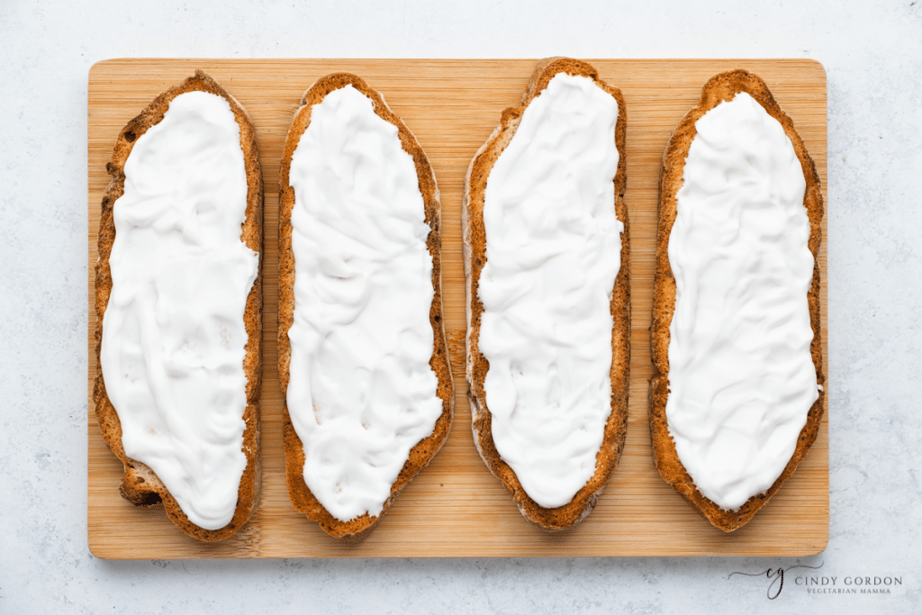 wooden cutting board with long bread slices with white mixture on it