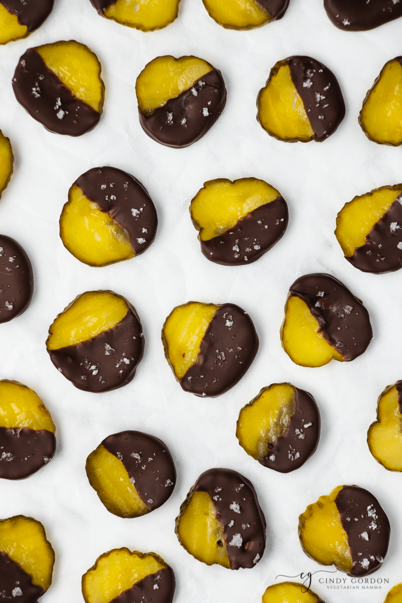 overhead shot of green pickle circles with half pickle showing, other half dipped into dark brown chocolate with white sea salt flakes
