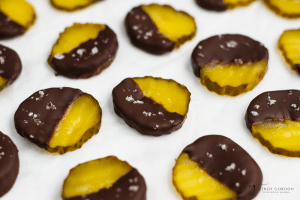 angled shot of green pickle circles with half pickle showing, other half dipped into dark brown chocolate with white sea salt flakes