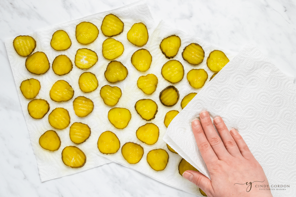 hand patting a papertowel on top of green pickle circles