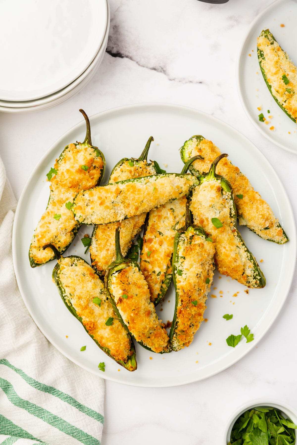 up close shot o white plate full of sliced open jalapeno peppers that are stuffed with white and green cream cheese and golden brown breading.