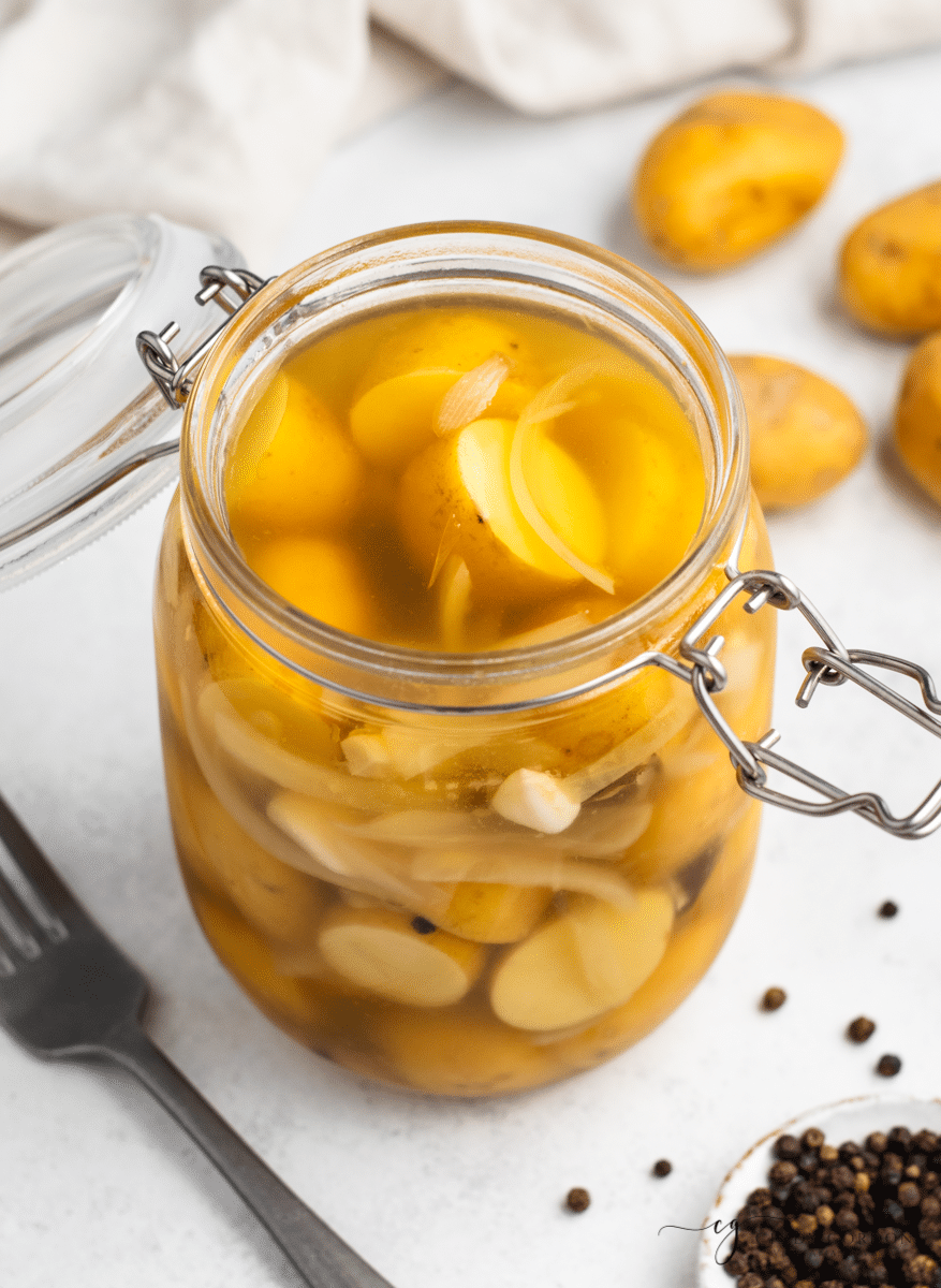 clear glass jar with yellow baby round potatoes cut in half with thin white onion slices in milkly liquid. vertical picture