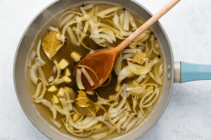 cooked onion slices with liquid and wooden spoon in a pot