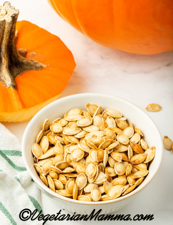 orange pumpkin at top with lid cut off, seeds cooked in bowl on a white background