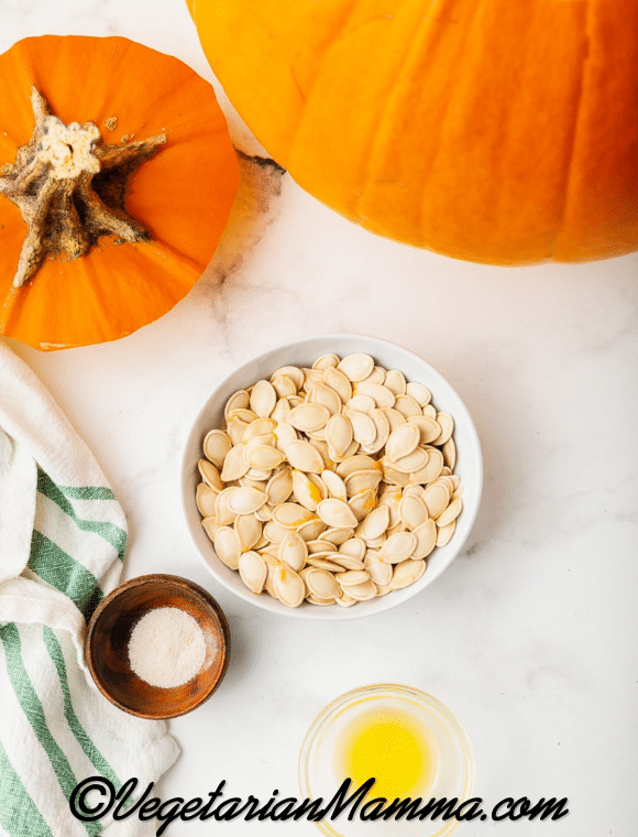 Overhead ingredient shot for air fryer pumpkin seeds, orange pumpkin, seeds in white bowl, salt, and melted butter