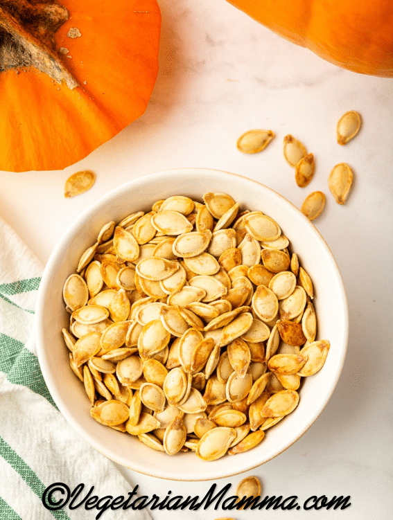 orange pumpkin at top with lid cut off, seeds cooked in a bowl on a white background
