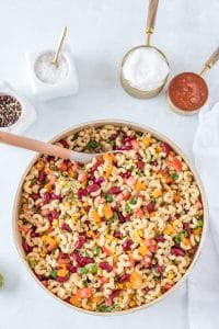 creamy macaroni salad with red, purple and green vegetables in it with wooden spoon in bowl
