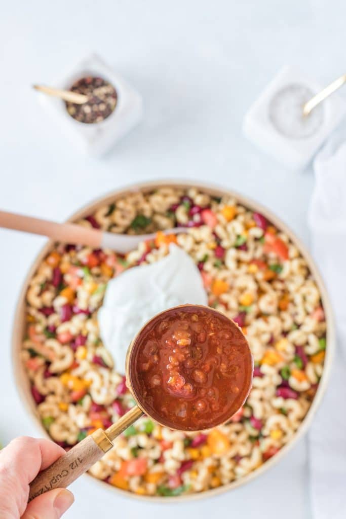 scoop of salsa on top of creamy macaroni salad with red, purple and green vegetables in it