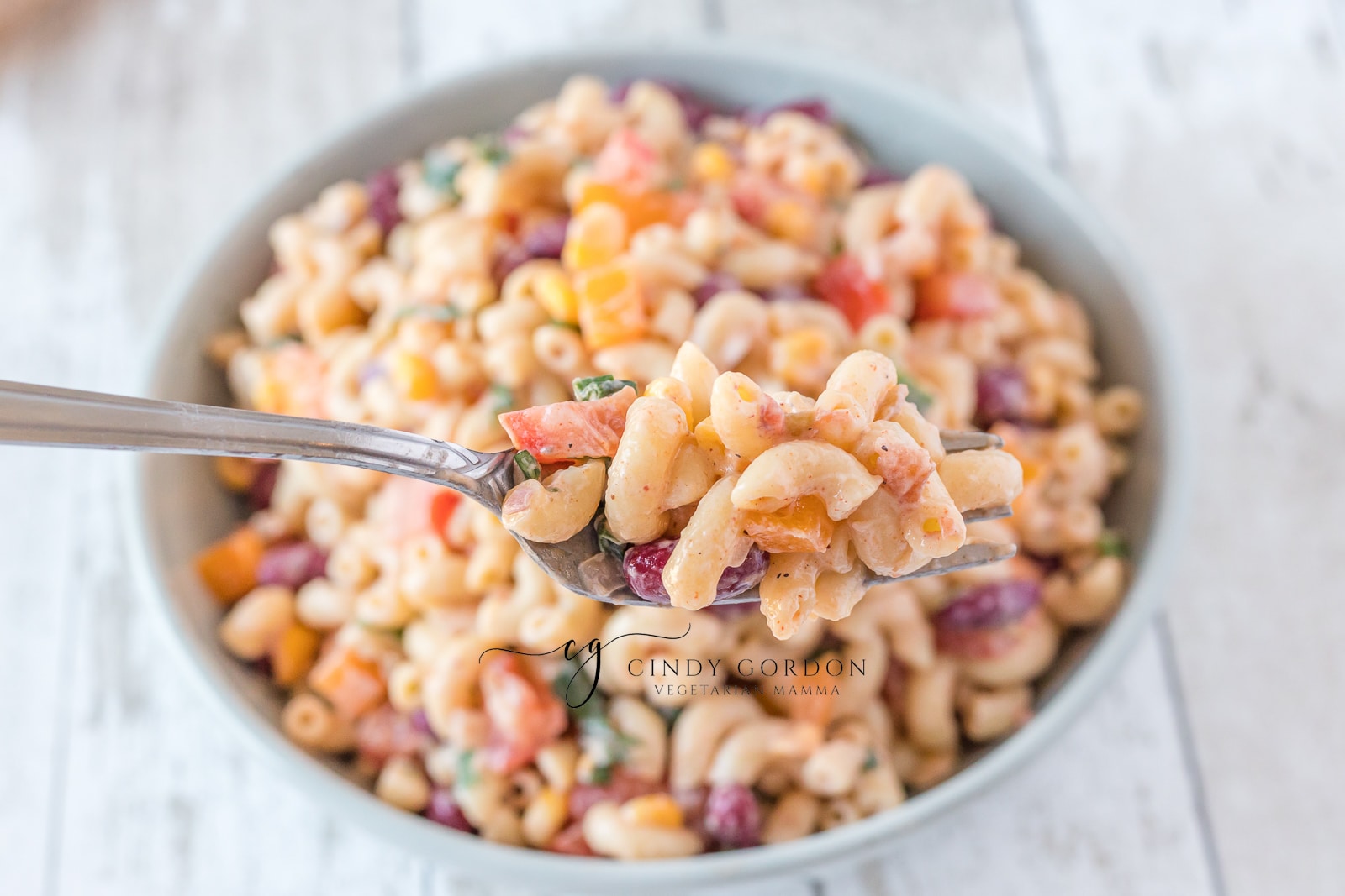creamy macaroni salad with red, purple and green vegetables in it in a blue bowl