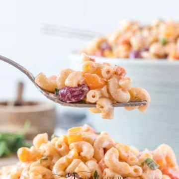 creamy macaroni salad with red, purple and green vegetables in it in a blue bowl fork with pasta salad on it