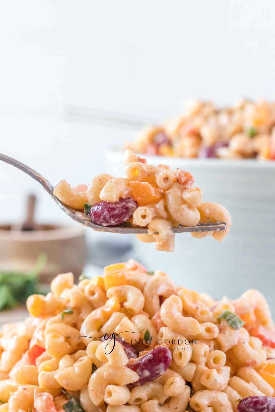creamy macaroni salad with red, purple and green vegetables in it in a blue bowl fork with pasta salad on it