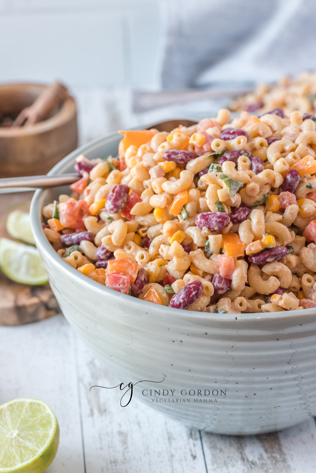 blue bowl filled with creamy macaroni salad with red, purple and green vegetables in it