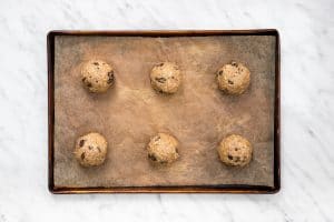 vegan oatmeal raisin cookies - brown fluffy cookies with dark brown raisins rolled into balls on a baking sheet
