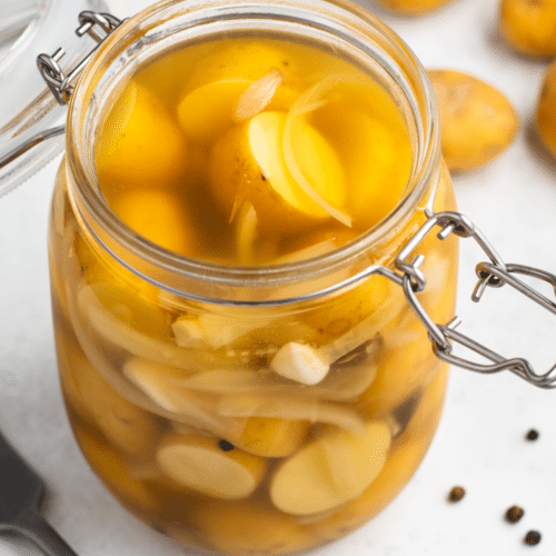 pickled potatoes feature image, glass clear jar with yellow tiny circle potatoes, milky liquid and white onion slices