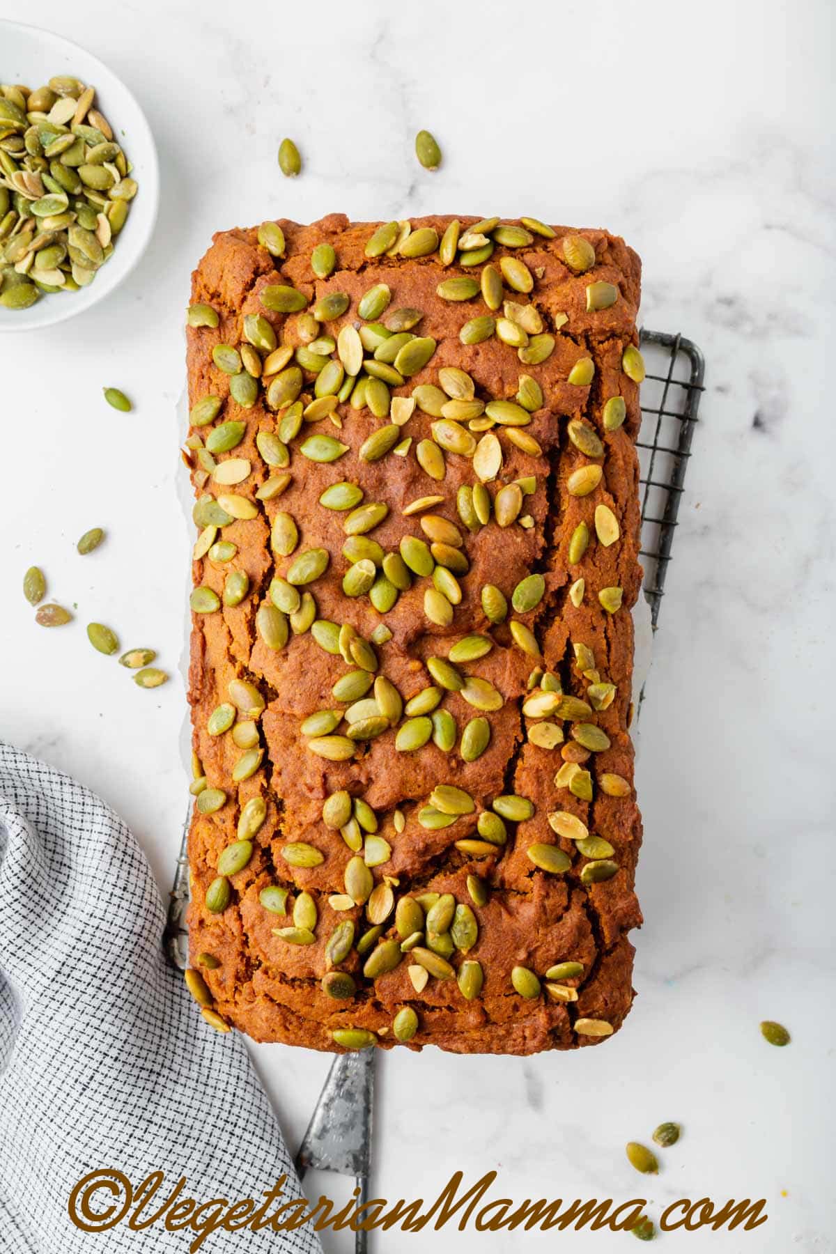 Overhead shot of a loaf of pumpkin bread garnished with seeds on a wire cooling rack