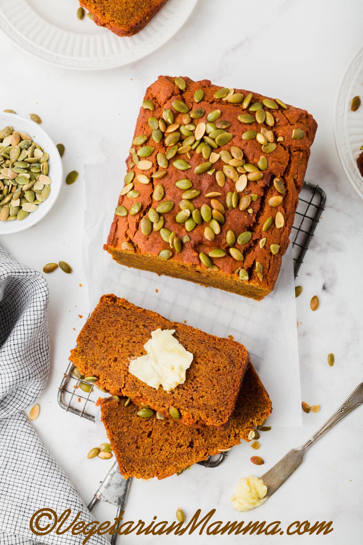 lices of pumpkin bread with butter next to a loaf of bread garnished with pumpkin seeds