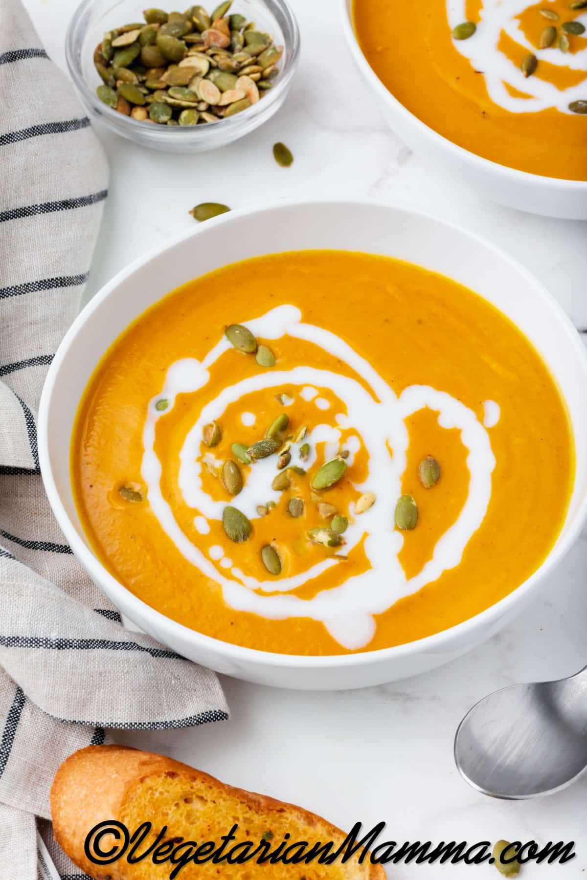 2 bowls of vegan pumpkin soup garnished with coconut milk and pumpkin seeds