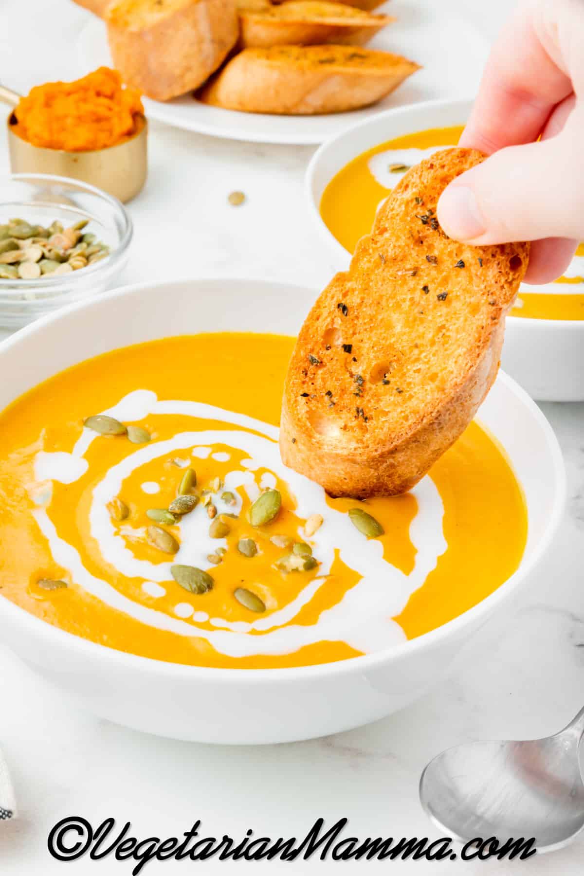 A hand dipping crunchy bread into a white bowl of pumpkin soup