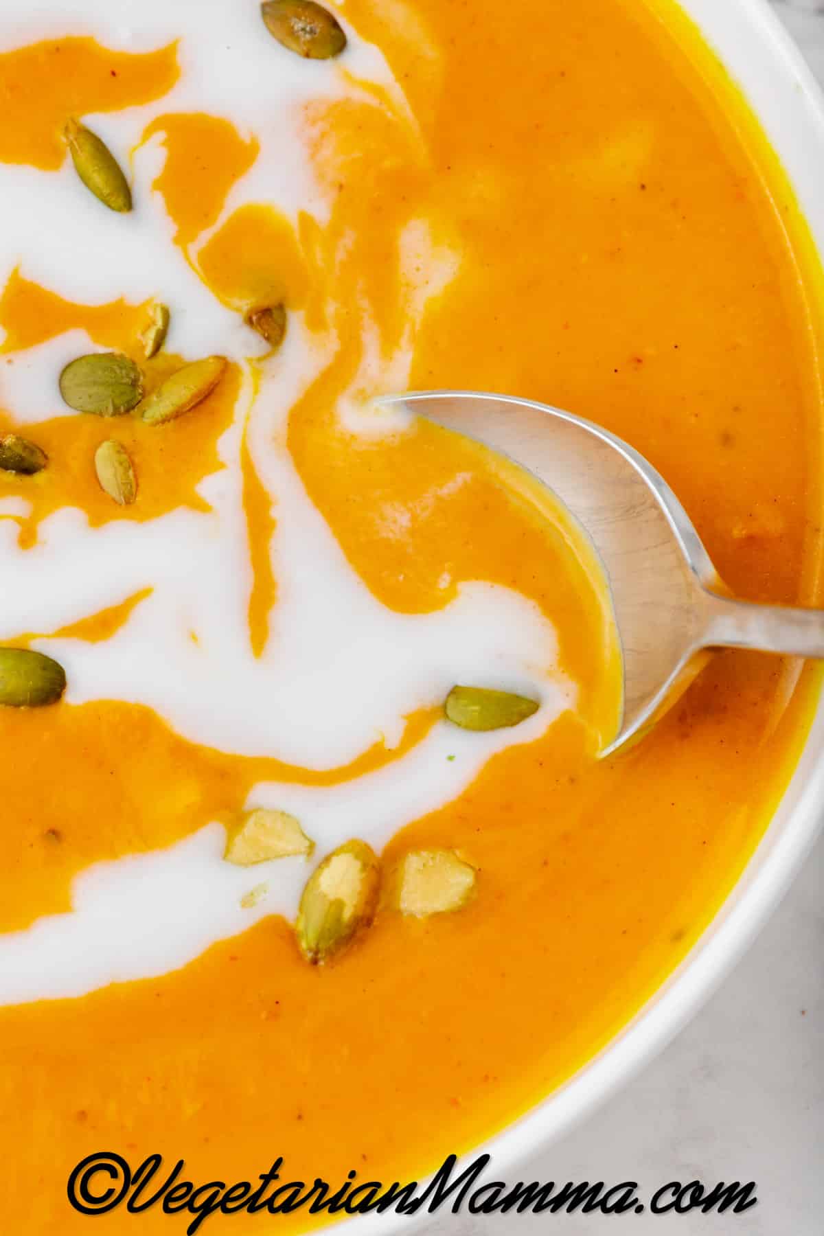 Close-up shot of a silver spoon in a bowl of pumpkin soup with coconut milk