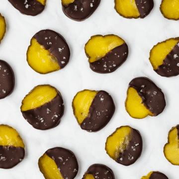 green pickle circles with half pickle showing, other half dipped into dark brown chocolate with white sea salt flakes on a white piece of parchment paper