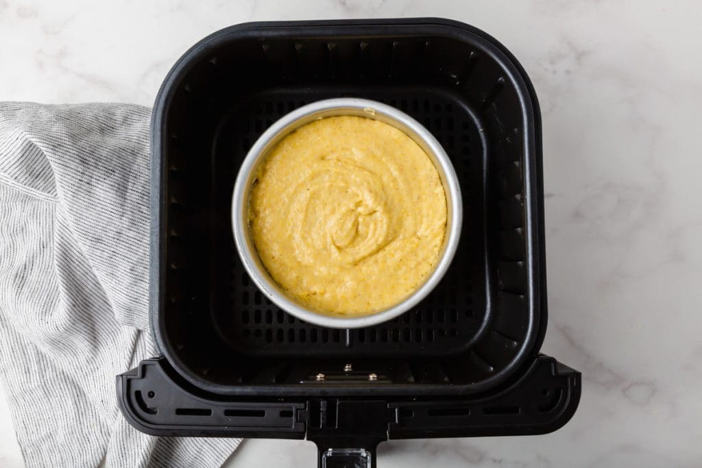 yelllow liquid and flour mixed together in a metal round container in a black air fryer basket
