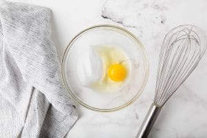 egg and clear liquid in a clear glass bowl with whisk to the right