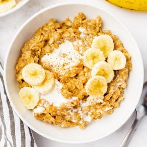 white bowl with golden brown oats with some white milk. Yellow sliced bananas on top